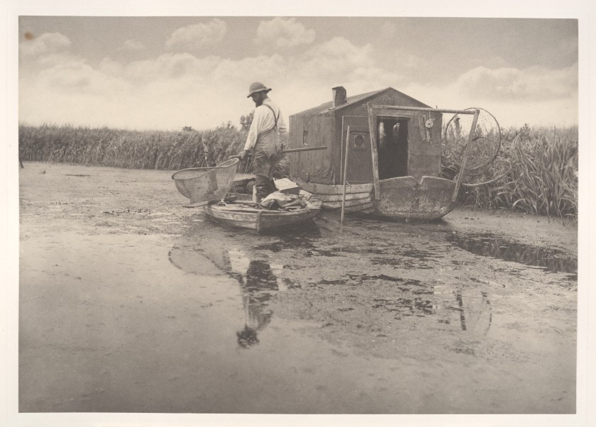 Se trata de una fotografía de Penter Henry Emerson, tomada entre 1885 y 1886, presumiblemente en el dominio público por su antigüedad, titulada " An Eel-Catcher's Home" (El hogar de un pescador de anguilas), donada al museo en 2008 por Joyce F. Menschel.